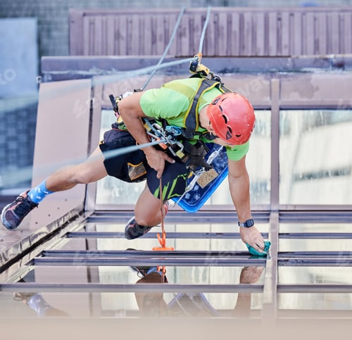 Preview: Industrial mountaineering worker cleaning window outside building.