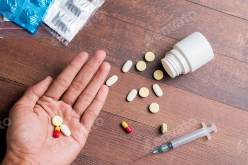 Preview: Hand Holding Pills with Syringe on Wooden Surface