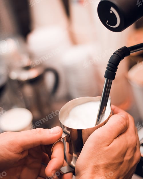 Preview: Person pouring a steady stream of milk into a cup of freshly brewed coffee using a metal pipe