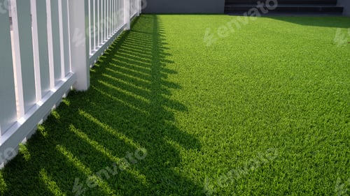 Preview: Sunlight and shadow of white wooden fence on green artificial turf surface in front yard of home