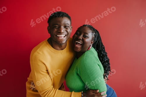 Preview: Beautiful young African couple embracing and smiling while standing on red background together