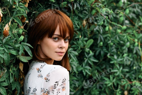 Preview: Vibrant redhaired woman standing in front of lush green plant wall