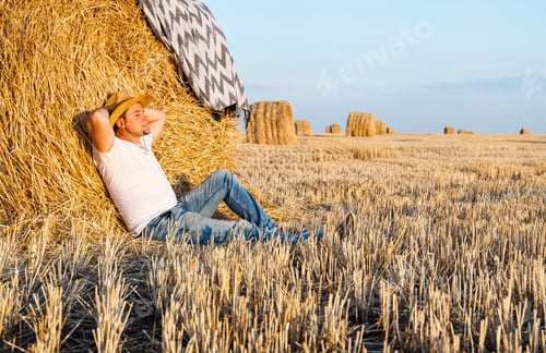 Preview: Cute man resting after hay harvesting in haystacks