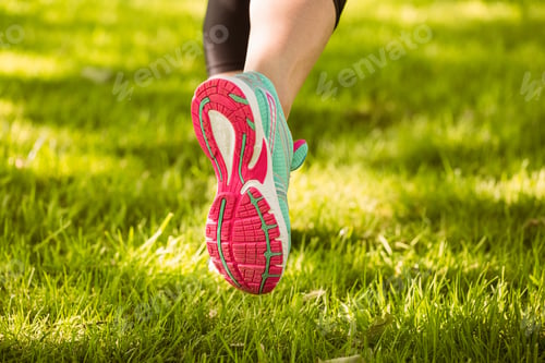 Preview: Woman in running shoes running on grass in the park