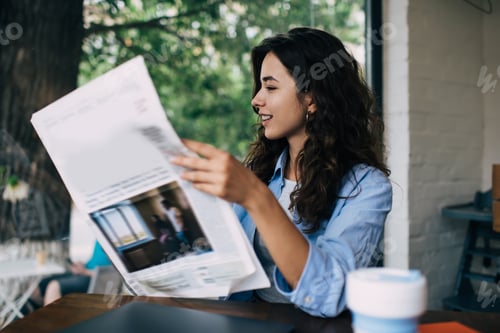Preview: Young woman reading newspaper in cafe