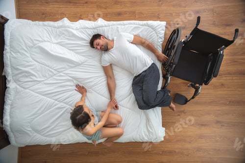 Preview: The woman sitting near the disabled man on the bed. view from above