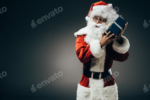 Preview: shocked santa claus in costume listening gift box isolated on grey background