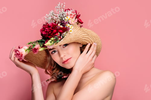 Preview: attractive naked woman in hat with flowers looking at camera isolated on pink