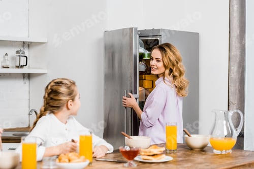 Preview: girl sitting at table and looking at mother opening fridge