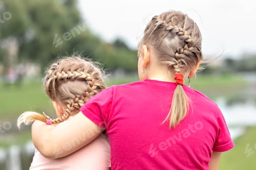 Preview: Two little girls, sisters are sitting in an embrace. Identical hairstyles, braids.