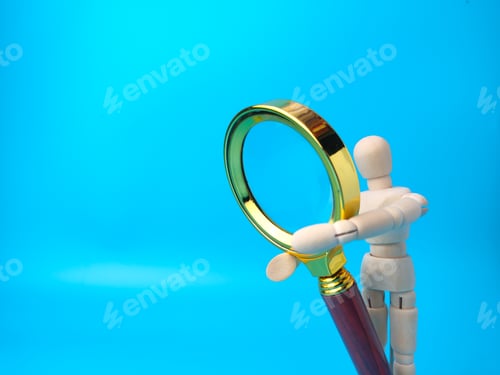 Preview: Wooden mannequin holding vintage magnifying glass on a blue background with copy space.