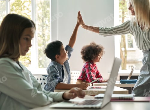 Preview: Happy teacher giving high five to boy in class with group of schoolchildren.