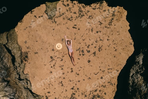 Preview: Tanned young lady relaxing on rocky coast in summer
