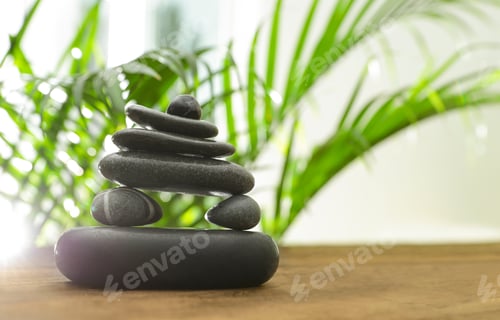 Preview: Table with stack of stones and blurred green leaves on background, space for text. Zen concept