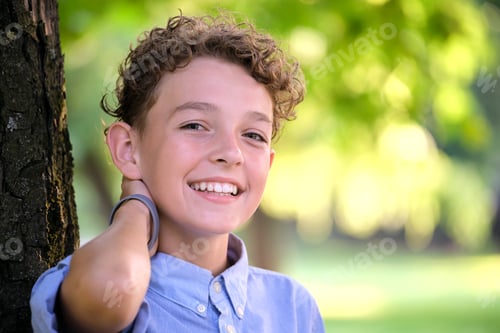 Preview: Young happy child boy relaxing in summer park leaning on tree trunk. Child wellbeing concept