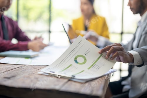 Preview: A man is pointing at a pie chart on a table in front of three other people.
