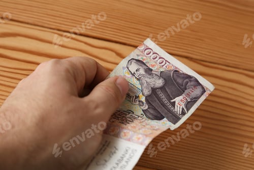 Preview: High angle shot of a person holding some cash over a wooden surface