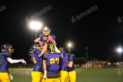 Preview: American football team celebrating victory on field at night