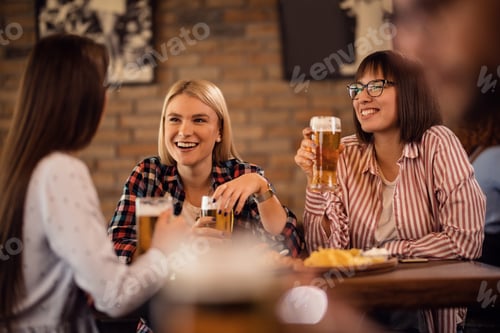 Preview: Happy female friends drinking beer and talking in a pub.