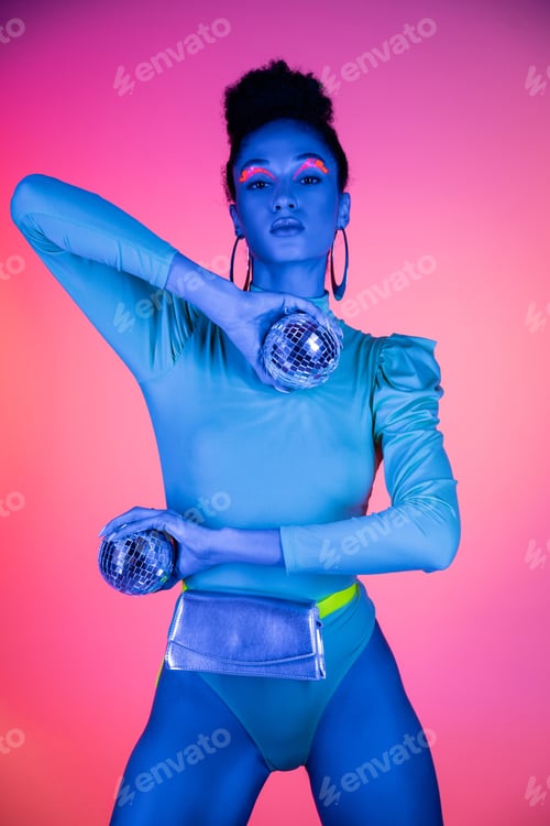Preview: Trendy african american woman with neon visage holding disco balls on pink background