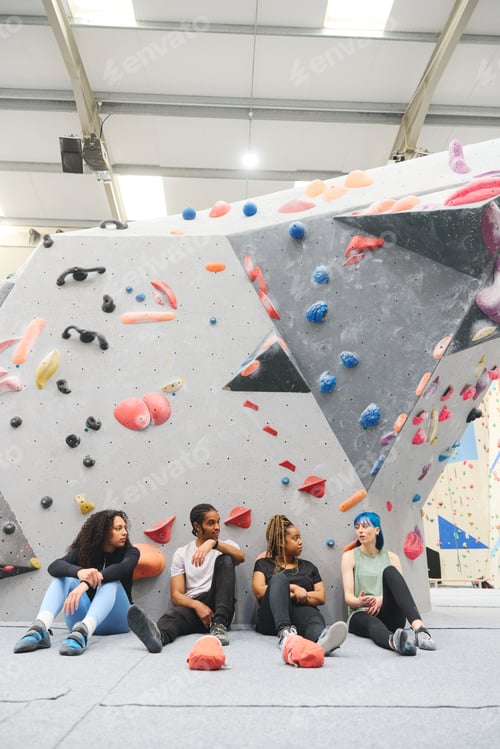 Preview: Group Of Friends Sitting On Floor Taking A Break After Exercise At Indoor Wall Climbing Centre