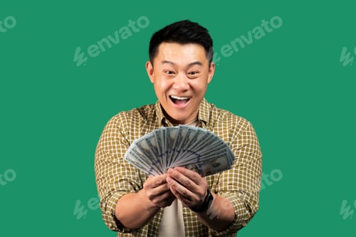 Preview: Excited korean man holding fan of money cash in hands and looking at it with open mouth, posing on