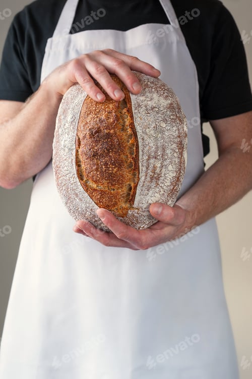 Preview: Close-up at bakers hands holding a loaf of bread in front of him.