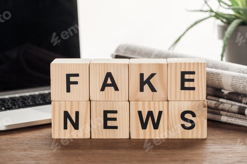 Preview: wooden cubes with words fake news, plant, laptop and newspapers on wooden tabletop