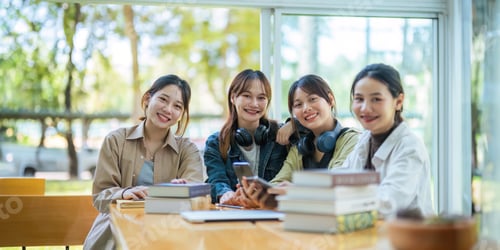 Preview: University students sitting together at table with book and laptop. Happy young people doing group