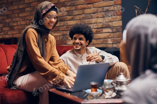 Preview: Happy Muslim woman using laptop while studying with friends in a cafe.