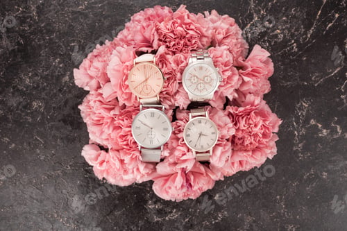 Preview: top view of elegant wristwatches lying on blooming pink flowers on grey surface