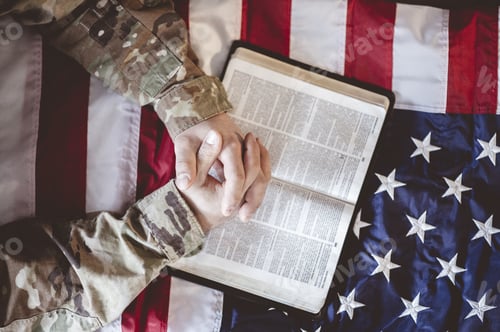 Preview: American soldier mourning and praying with the Bible in his hands and the American flag