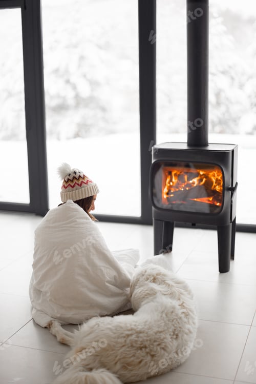 Preview: Woman with dog at home with burning fireplace during wintertime