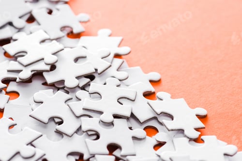 Preview: selective focus of unfinished white jigsaw puzzle pieces on orange
