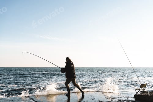 Preview: Silhouette of man fisherman wearing coat, holding rod
