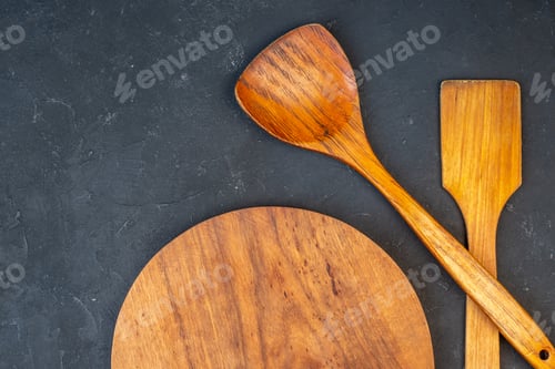Preview: top half view wooden round board wooden spoons on dark background