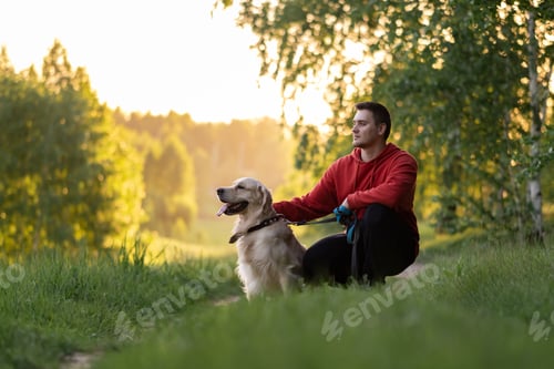 Preview: Young man with a golden retriever for a walk in a summer park.