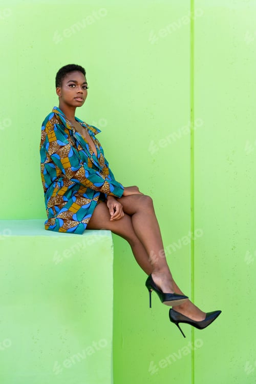 Preview: Black female in traditional African suit and sitting against pistachio background