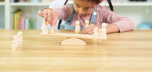 Preview: Unidentified little girl is trying how to balance the wooden people model on the scale.
