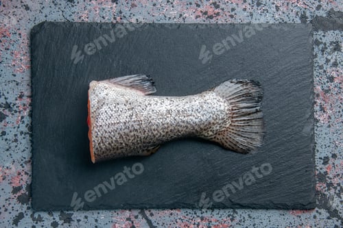 Preview: Overhead view of fresh raw fish on dark color tray on blue black mix colors background