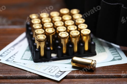 Preview: Many metal cartridges, dollars and ammunition belt on wooden table, closeup