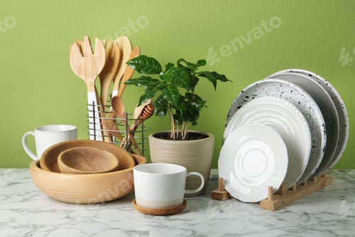 Preview: Potted plant and set of kitchenware on white marble table near green wall. Modern interior design