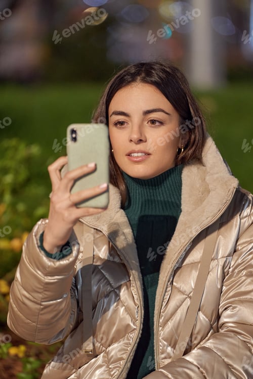 Preview: Woman in winter jacket using a mobile phone while sitting outdoors.