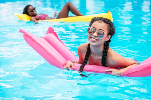 Preview: Young multiethnic women floating on inflatable mattresses in swimming pool at resort