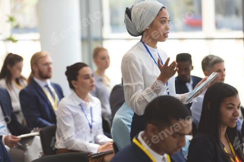 Preview: Young businesswoman with headscarf asking question during seminar in office building