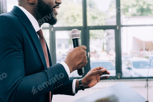 Preview: cropped image of smiling african american speaker talking into microphone during seminar in