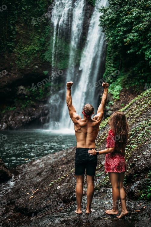 Preview: Tourists at the waterfall, rear view. Couple on vacation in Bali. Honeymoon trip