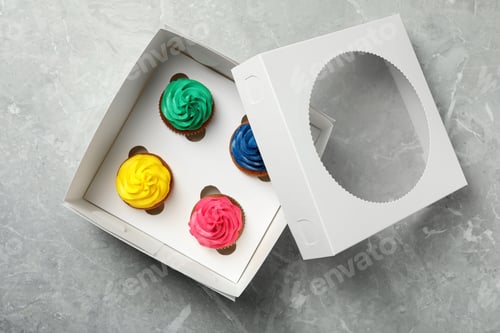 Preview: Box with different cupcakes on grey table, top view