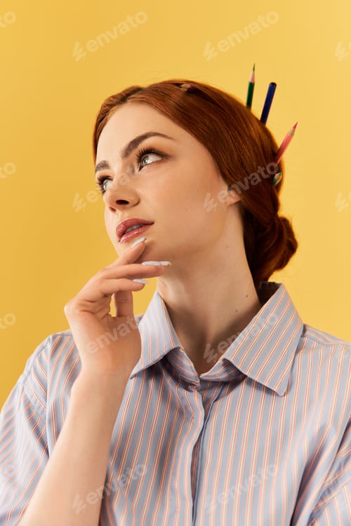 Preview: Young woman with red hair and pencils in her updo gazes thoughtfully while wearing a striped shirt