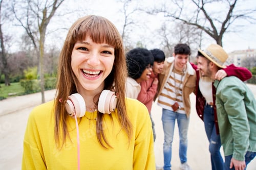 Preview: Young smiling girl looking at the camera outdoors with group of friends.